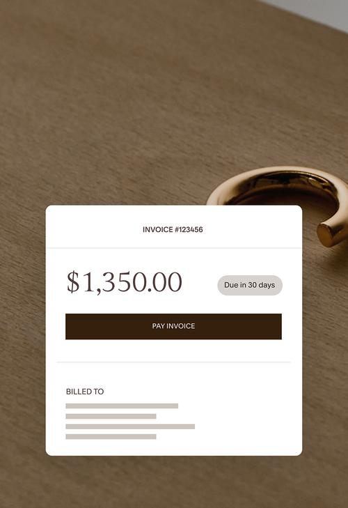 Online invoice for $1,350 due in 30 days with a pay invoice button, displayed beside gold jewelry on a wooden surface.