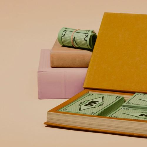 Stacks and rolls of money inside and around a book, displayed against a beige background.